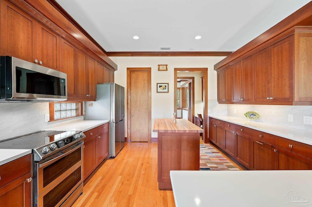 kitchen with a kitchen island, appliances with stainless steel finishes, crown molding, light hardwood / wood-style floors, and decorative backsplash