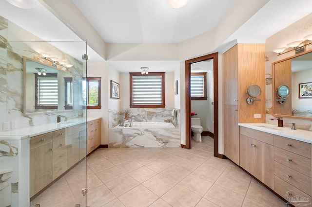 bathroom with tiled tub, vanity, toilet, and tile patterned flooring