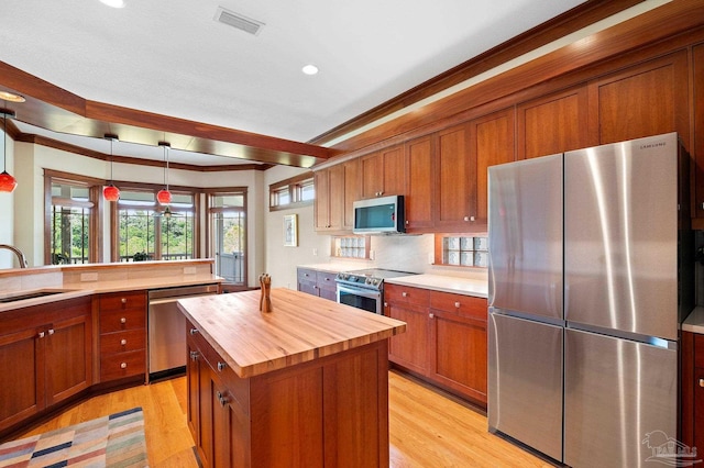 kitchen with hanging light fixtures, a kitchen island, stainless steel appliances, light wood-type flooring, and wood counters