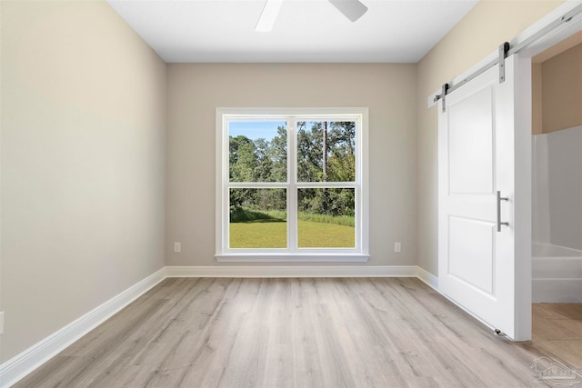 spare room featuring a barn door, ceiling fan, and light hardwood / wood-style flooring