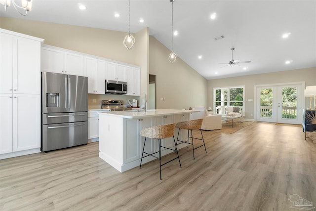 kitchen with ceiling fan with notable chandelier, stainless steel appliances, light hardwood / wood-style floors, an island with sink, and high vaulted ceiling