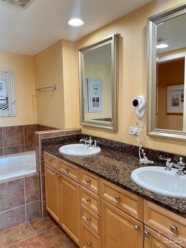 bathroom featuring tile patterned flooring, tiled bath, and double sink vanity