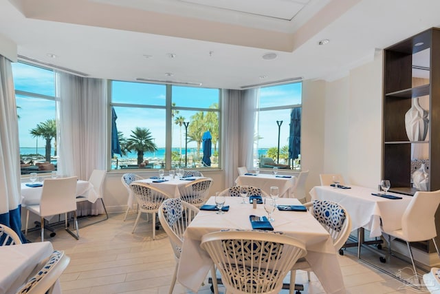 dining room featuring light hardwood / wood-style floors, a water view, and a raised ceiling