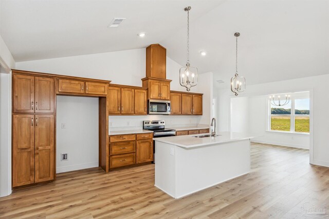 kitchen featuring an island with sink, sink, hanging light fixtures, stainless steel appliances, and light hardwood / wood-style flooring