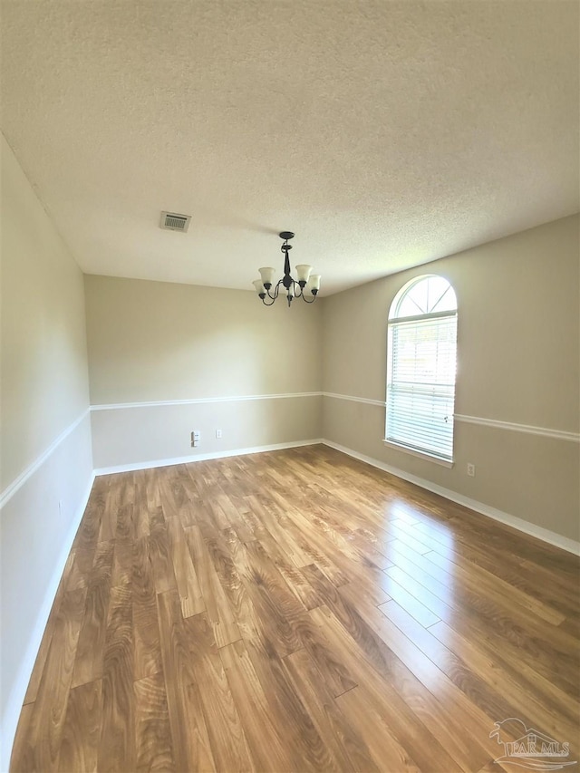 unfurnished room with a chandelier, hardwood / wood-style floors, and a textured ceiling