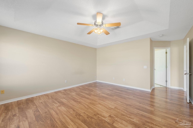 empty room featuring hardwood / wood-style flooring, a textured ceiling, a raised ceiling, and ceiling fan