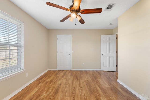 spare room featuring ceiling fan, a wealth of natural light, a textured ceiling, and light wood-type flooring