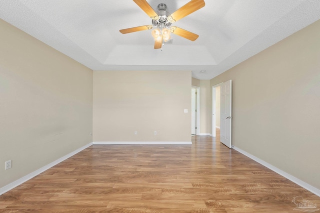 spare room with ceiling fan, light hardwood / wood-style floors, a textured ceiling, and a tray ceiling