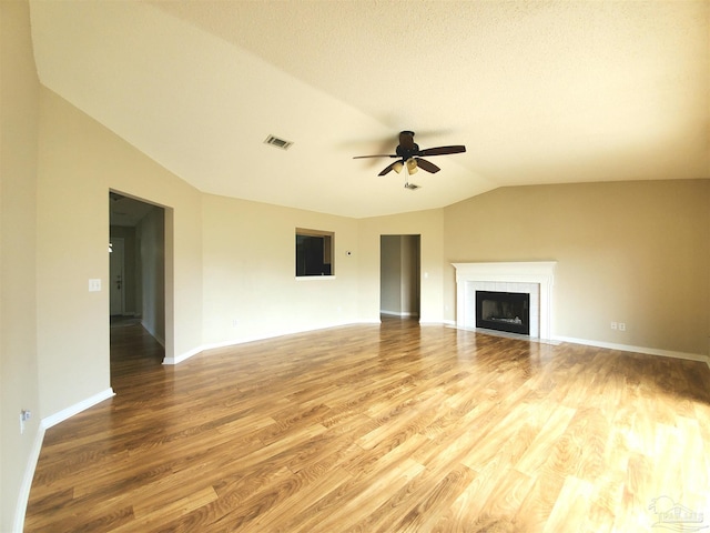 unfurnished living room featuring ceiling fan, wood-type flooring, a textured ceiling, a tiled fireplace, and vaulted ceiling