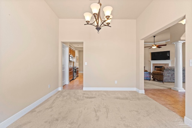 spare room featuring ceiling fan with notable chandelier, ornate columns, and light carpet