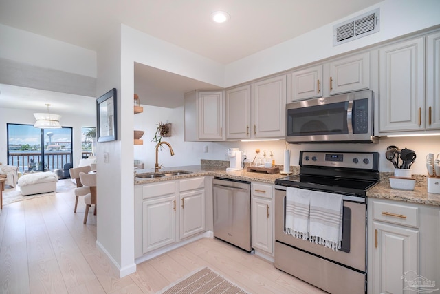 kitchen with stainless steel appliances, sink, light stone countertops, an inviting chandelier, and light wood-type flooring