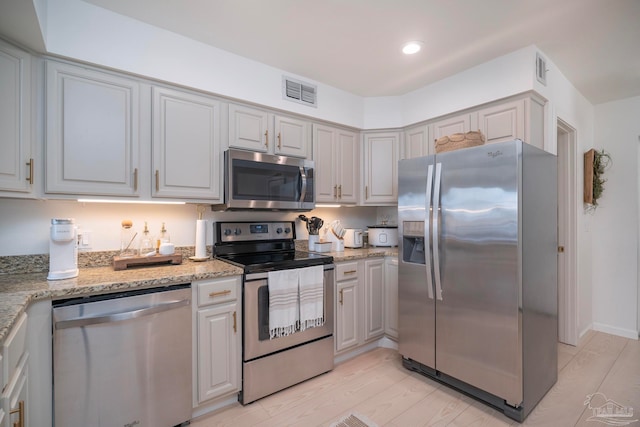 kitchen with appliances with stainless steel finishes, light hardwood / wood-style flooring, and light stone countertops