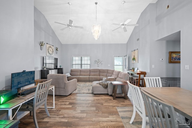 living room with ceiling fan with notable chandelier, high vaulted ceiling, and light hardwood / wood-style floors