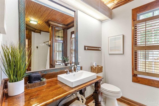 bathroom featuring toilet, a sink, a shower with curtain, wooden ceiling, and baseboards