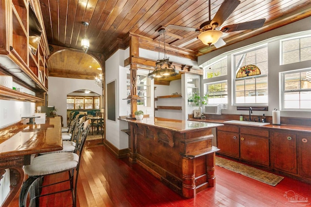 kitchen featuring arched walkways, dark wood-type flooring, a ceiling fan, wood ceiling, and a sink