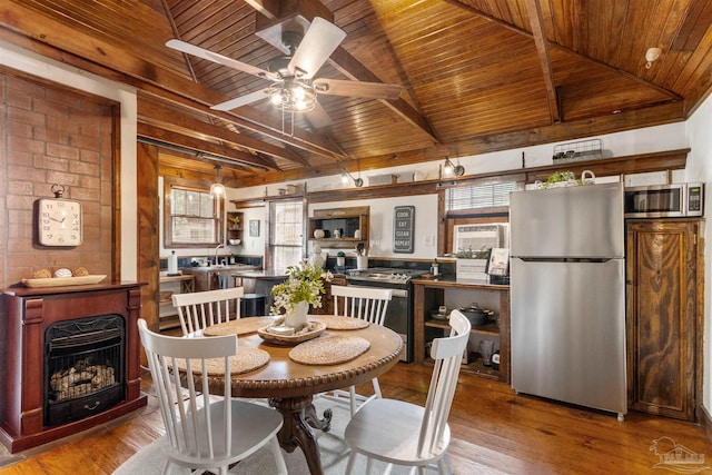 dining room with vaulted ceiling with beams, light wood-type flooring, wooden ceiling, and a fireplace