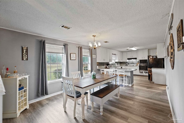 dining space with an inviting chandelier, a textured ceiling, and wood-type flooring