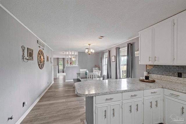 kitchen with light hardwood / wood-style flooring, hanging light fixtures, kitchen peninsula, white cabinetry, and a textured ceiling