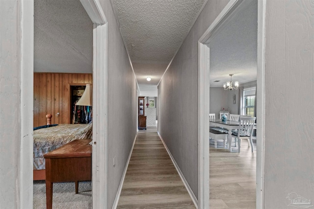 hallway featuring a notable chandelier, a textured ceiling, hardwood / wood-style flooring, and wooden walls