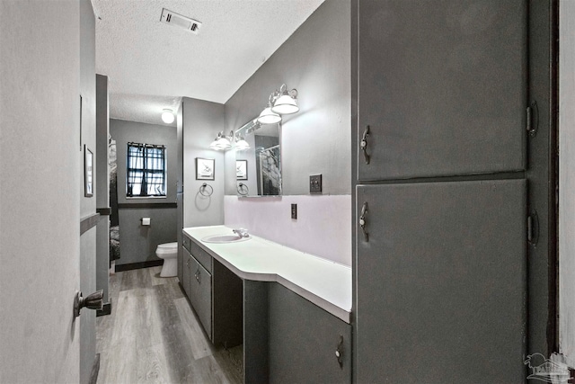 bathroom featuring a textured ceiling, hardwood / wood-style floors, toilet, walk in shower, and vanity