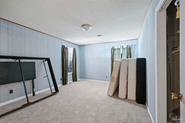 bedroom with a textured ceiling, light colored carpet, and wood walls