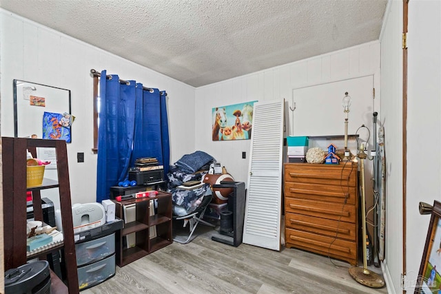 miscellaneous room with light hardwood / wood-style floors, a textured ceiling, and wooden walls