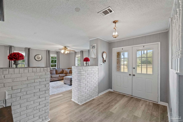 entrance foyer featuring french doors, a textured ceiling, ceiling fan, crown molding, and light hardwood / wood-style flooring