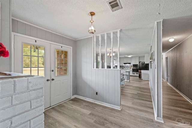 entryway featuring french doors, light hardwood / wood-style flooring, crown molding, a textured ceiling, and wood walls