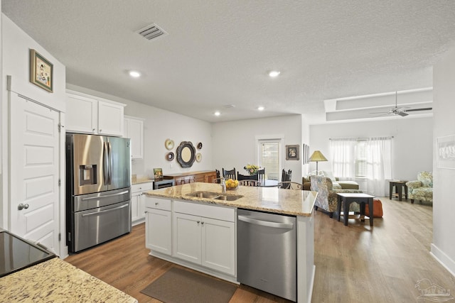 kitchen with sink, wood-type flooring, stainless steel appliances, a kitchen island with sink, and white cabinets