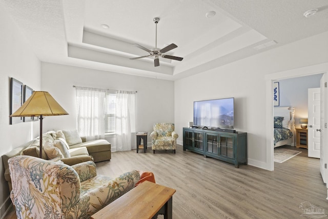 living room with ceiling fan, wood-type flooring, and a tray ceiling