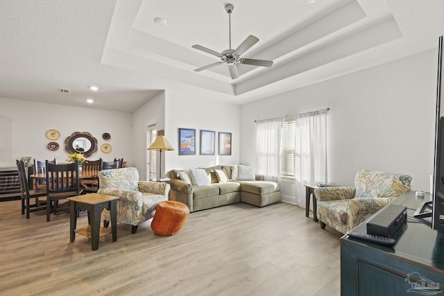 living room with light hardwood / wood-style flooring, ceiling fan, and a tray ceiling