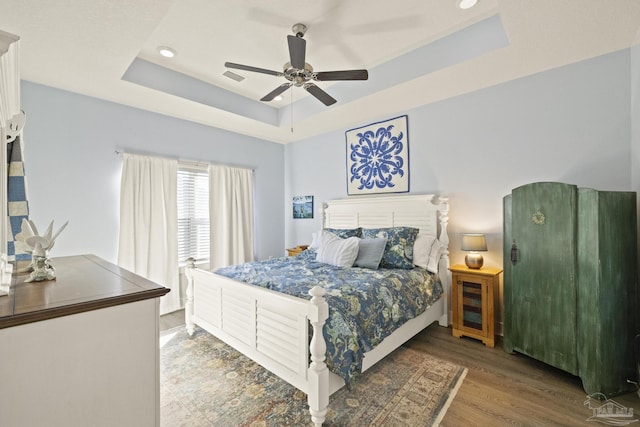 bedroom with dark wood-type flooring, a raised ceiling, and ceiling fan