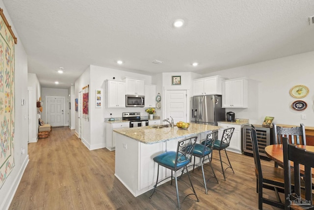 kitchen with a breakfast bar area, stainless steel appliances, light stone counters, white cabinets, and a center island with sink