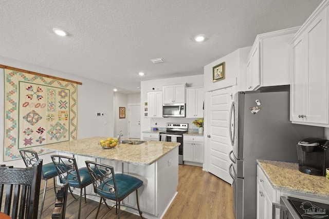 kitchen featuring white cabinetry, appliances with stainless steel finishes, light stone countertops, and a breakfast bar area