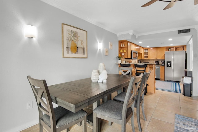 tiled dining area with ceiling fan and ornamental molding