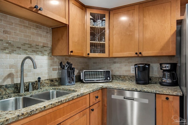 kitchen with light stone countertops, dishwasher, backsplash, and sink