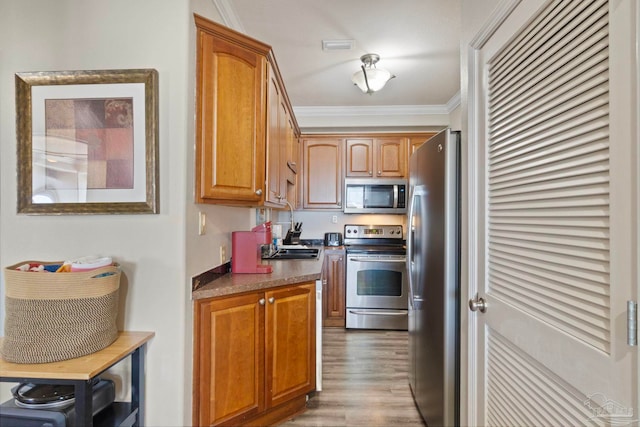 kitchen featuring dark countertops, ornamental molding, brown cabinets, appliances with stainless steel finishes, and wood finished floors