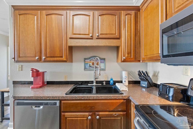 kitchen with dark countertops, brown cabinetry, appliances with stainless steel finishes, and a sink
