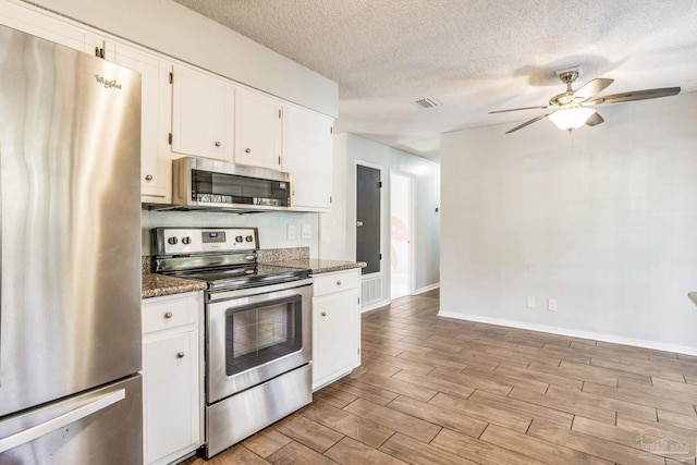 kitchen featuring white cabinets, stainless steel appliances, and dark stone counters