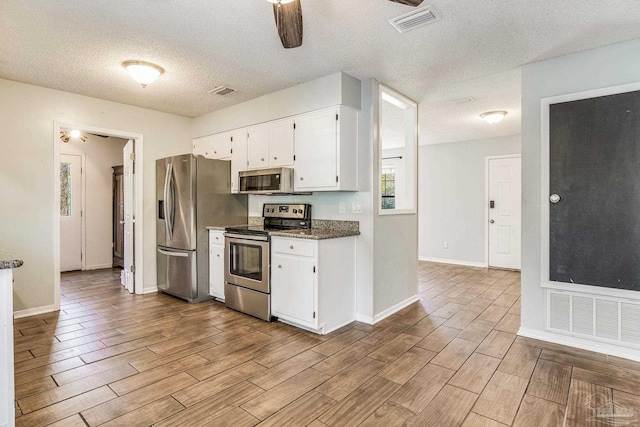 kitchen featuring appliances with stainless steel finishes, dark stone countertops, white cabinets, ceiling fan, and a textured ceiling