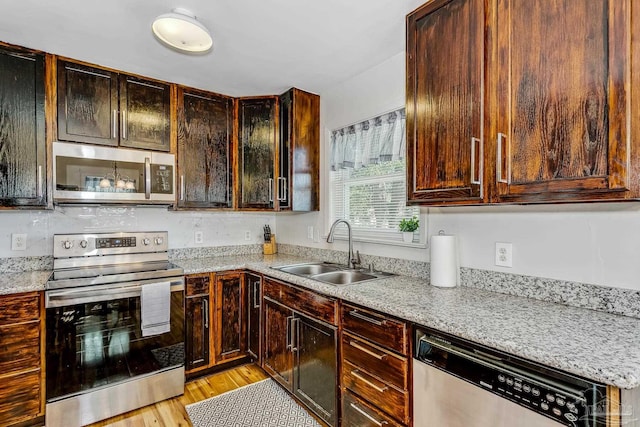 kitchen with light wood-type flooring, appliances with stainless steel finishes, light stone countertops, sink, and dark brown cabinetry