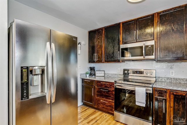 kitchen featuring dark brown cabinets, light stone counters, stainless steel appliances, and light hardwood / wood-style floors