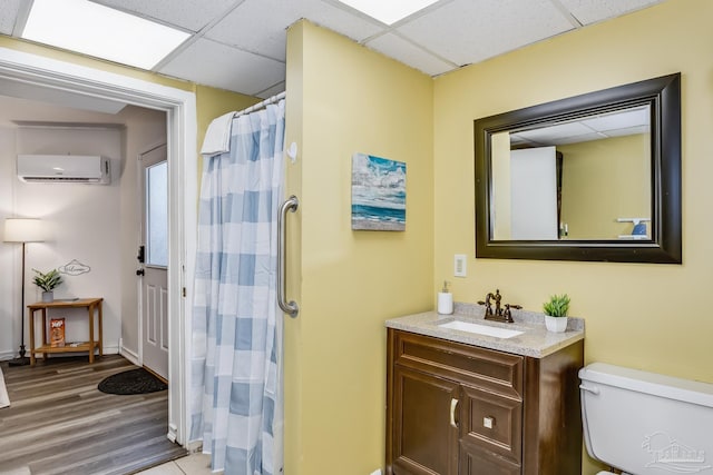 bathroom featuring toilet, vanity, hardwood / wood-style flooring, a paneled ceiling, and an AC wall unit