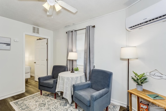 sitting room with dark wood-type flooring, a textured ceiling, a wall unit AC, and ceiling fan