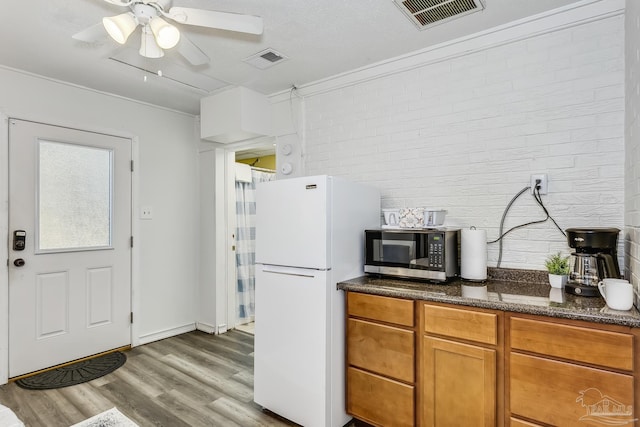 kitchen with white refrigerator, hardwood / wood-style floors, brick wall, dark stone counters, and ceiling fan