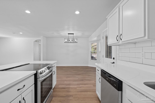 kitchen with decorative light fixtures, light hardwood / wood-style floors, white cabinetry, appliances with stainless steel finishes, and light stone counters