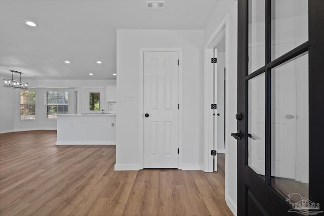 hallway with light wood-type flooring and a chandelier