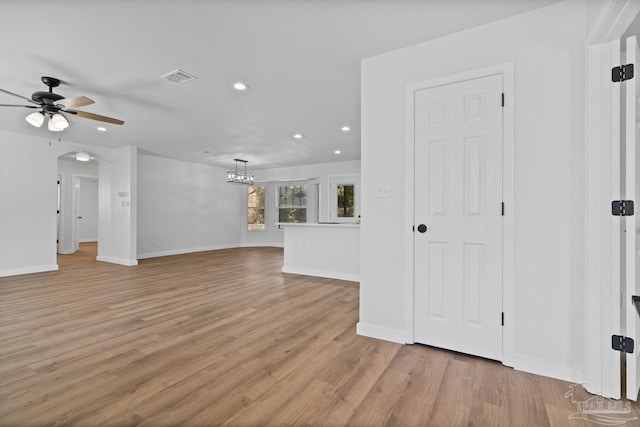 unfurnished living room with ceiling fan with notable chandelier and light hardwood / wood-style flooring