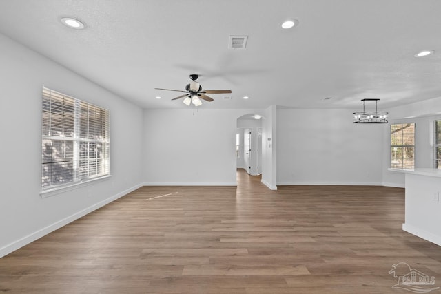 unfurnished living room featuring wood-type flooring and ceiling fan with notable chandelier