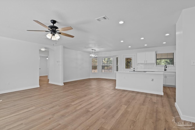 unfurnished living room with light wood-type flooring, ceiling fan with notable chandelier, plenty of natural light, and sink